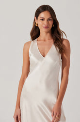 A woman is wearing a sleeveless, satin dress with a V-neckline. The dress is ivory or cream-colored with a smooth, shiny texture. She accessorized with large gold hoop earrings and a gold ring on her right hand.